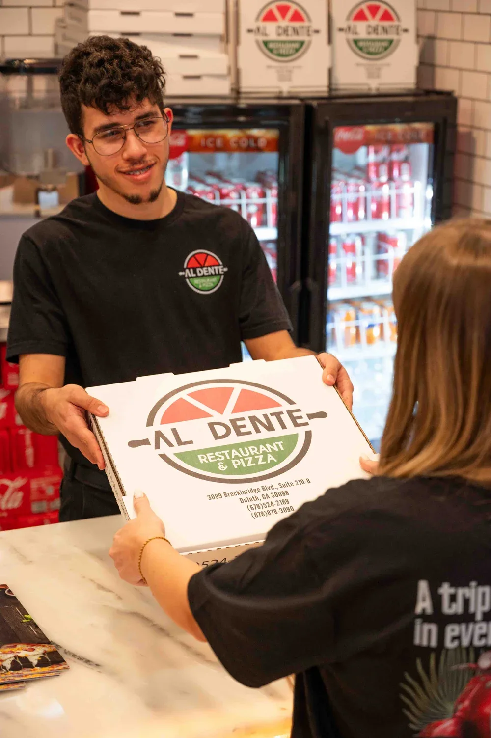 A team member handing a pizza box across the counter to a guest